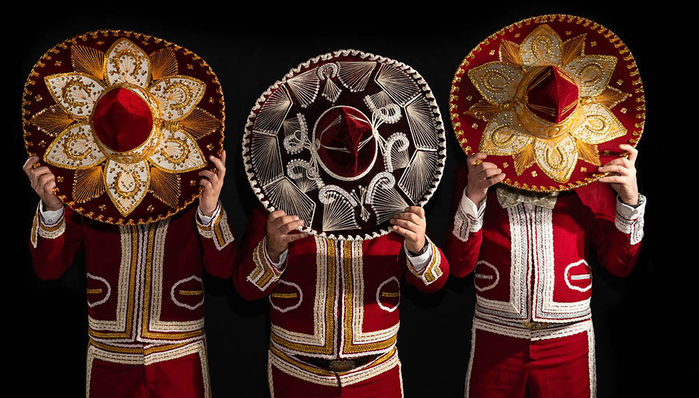 three mariachi guys holding their hats in front of their faces